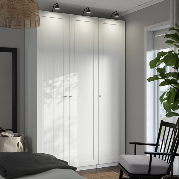 A white ikea PAX wardrobe with four doors in a modern bedroom. Its tall and narrow, fitting well against a grey wall.