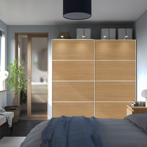 Minimalist bedroom with large PAX wardrobe. Modern light wood, sliding doors, mirrors, blue bed, grey walls.