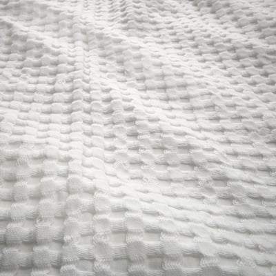 Close-up of a white waffle-weave bedspread showcasing its textured surface and soft cotton material.