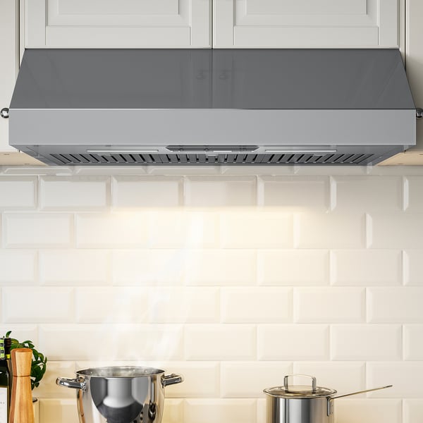Modern stainless steel kitchen hood with led light under white cabinets.