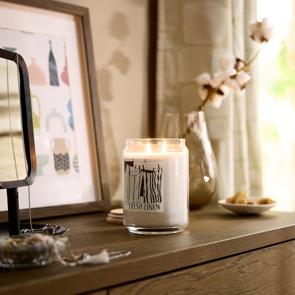 Decorated wooden table with a PRAKTHÄGER candle, white with black label, near a small vase, picture frame, and jewellery.