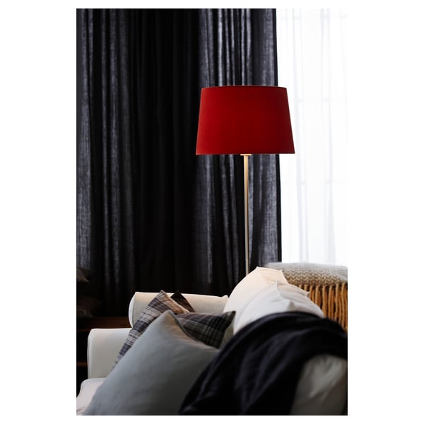 Dark room with red lamp on tall stand beside bed, curtains drawn, grey and white bedding.