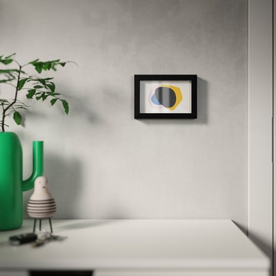 Modern wall art frame with colourful abstract design on a grey wall, displayed above a white table with a green vase and plant.