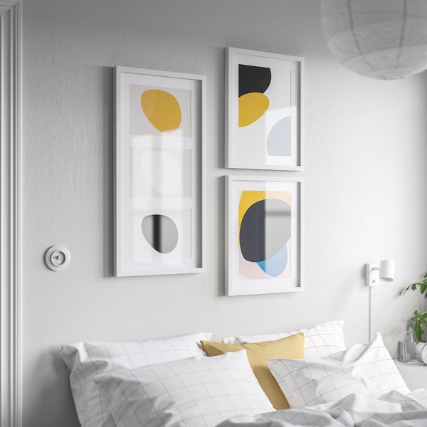 Three modern RÖDALM frames with abstract art hang above a bed with chequered pillows.
