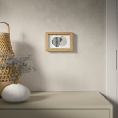 A minimalist room with abstract art on a grey wall, beige drawer, basket & flowers.