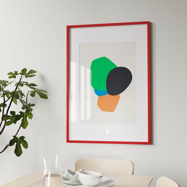 Modern red art print on grey wall above dining table with white dishes. Green plant to left.