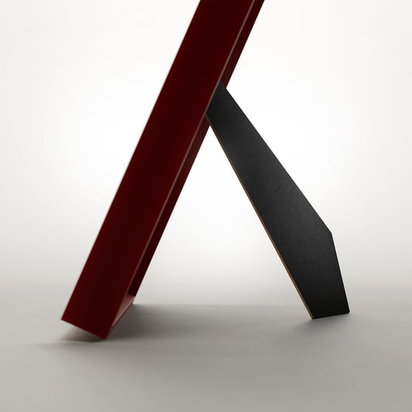 A red picture frame, standing upright, can be used with or without a mount, fitting various picture sizes.