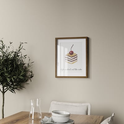 Framed cake artwork on wall, above wooden table with plant, bowl, and cup.