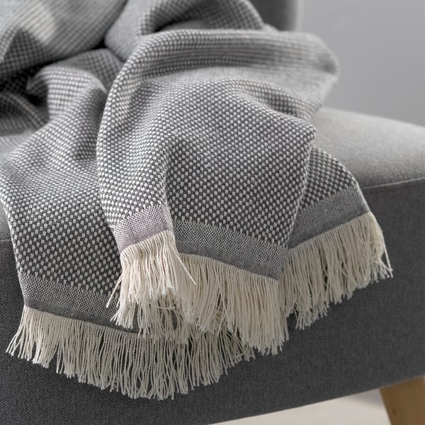 Cosy grey throw blanket with fringed edges draped on modern sofa, showcasing soft texture and high-quality materials.