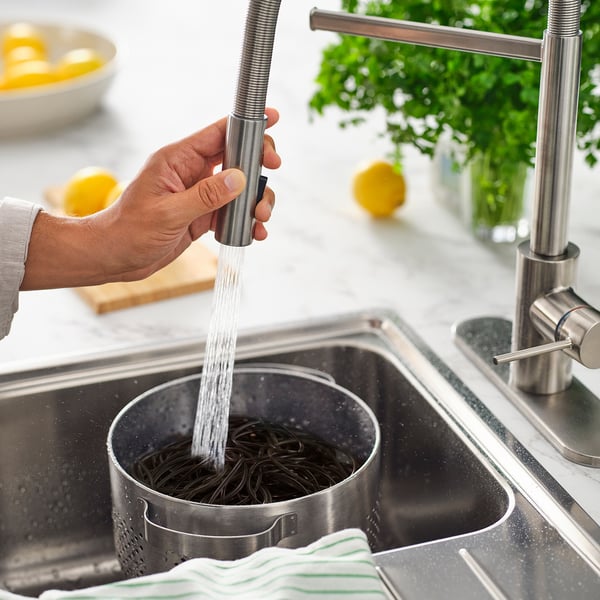 Person rinses pasta in colander under sleek, modern kitchen tap with pull-down spray.