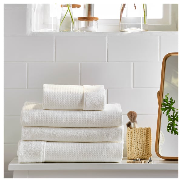 Clean, minimalist bathroom shelf with white SALVIKEN towels, neatly folded, alongside a woven basket, plant, and mirror.
