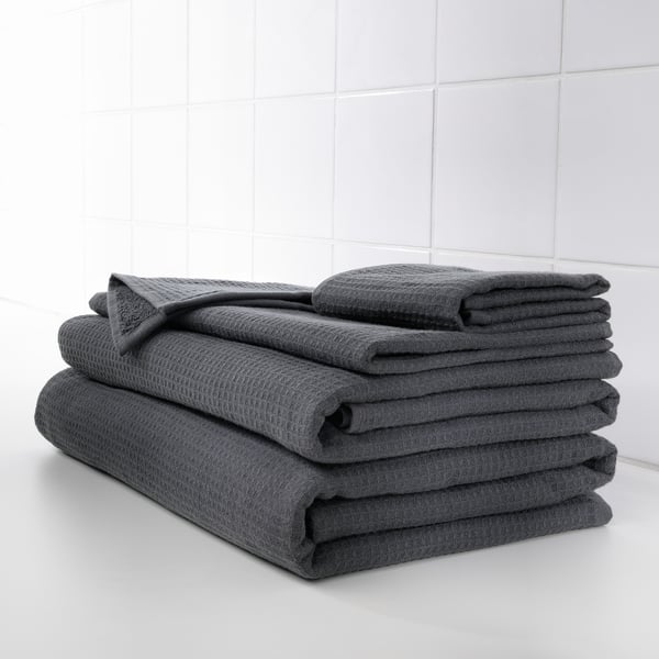 Neat stack of dark grey towels, folded carefully. Grey waffle texture on one side, soft terry on the other, placed on pristine white shelf.