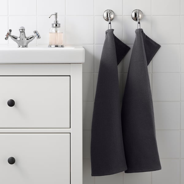 Modern bathroom with two grey SALVIKEN towels on silver hooks, textured sides. White sink cabinet with vintage tap and glass dispenser.