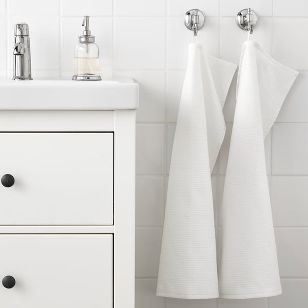 White bathroom with two towels hanging, one side terry, other waffle, on hooks beside a sink with soap dispenser.