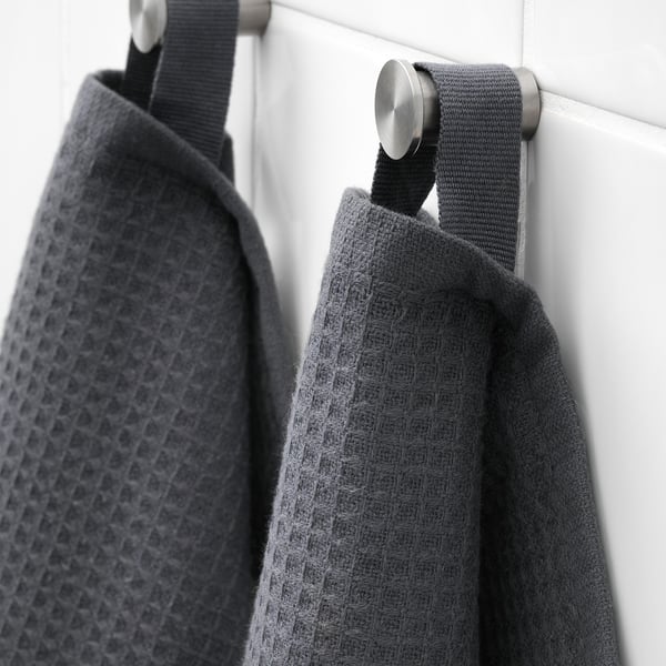 Two dark grey towels hang on hooks. One shows a waffle texture, the other soft terry, demonstrating absorbency and comfort.