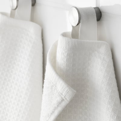 White towel hangers with soft, textured towels. One side is waffle-patterned; the other is terry. Mounted on a sleek, metallic holder.