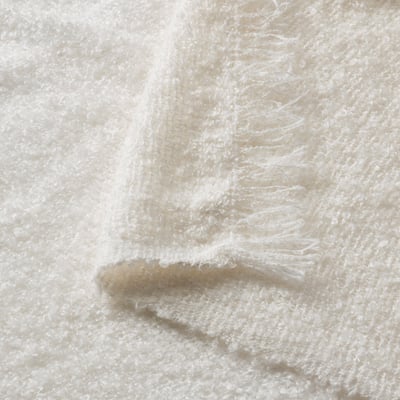 Close-up of soft, textured, off-white blanket showing crinkle-knit and fringe details.