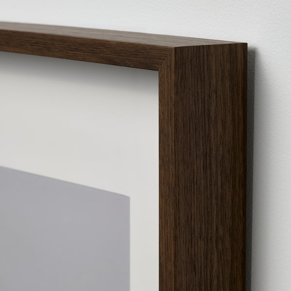 Close-up of a dark wooden picture frame corner, showing its smooth and polished finish, hard against a white wall.