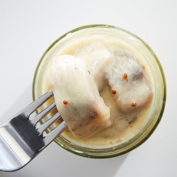 A jar of marinated herring in creamy mustard sauce, silver fork partially inserted.