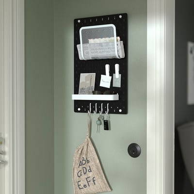 Black SKÅDIS pegboard organises office or home items. Holds notes, keys, and bag.