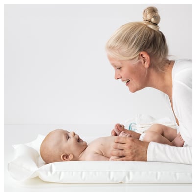 Person smiles tending to baby on white SKÖTSAM inflatable mat.