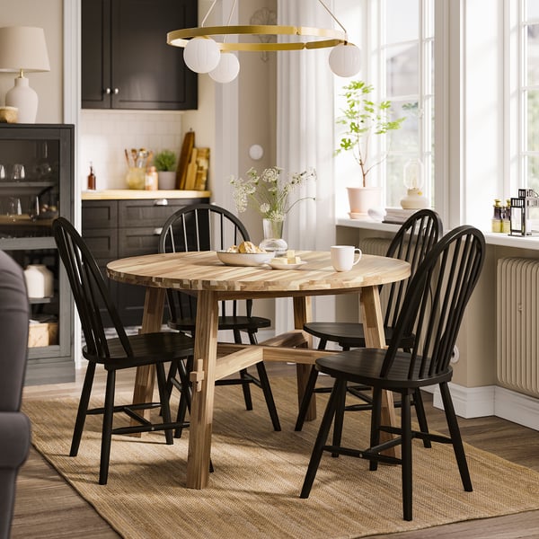 Small round SKOGSTA dining table with black chairs, set near a bright window, featuring a rustic wooden design.