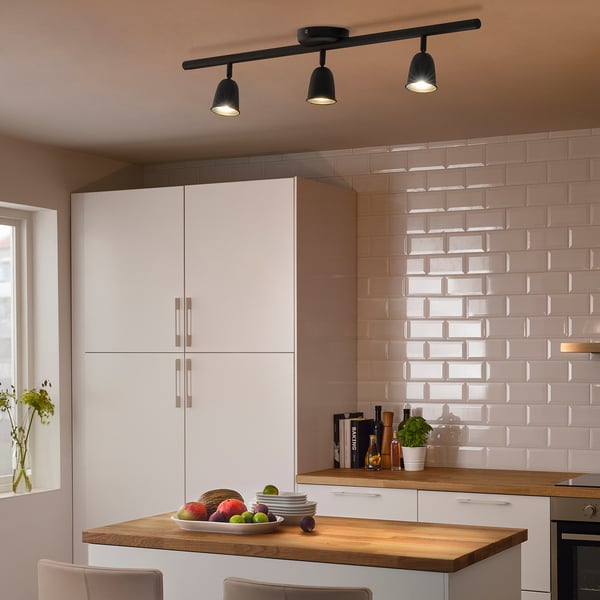 Modern kitchen with black ceiling lights, white cabinets, wooden counter.
