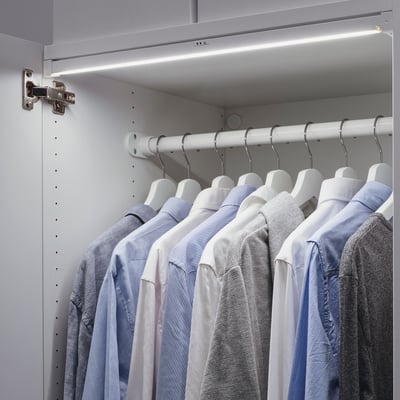 Closet with led lights above hanging shirts. Shirts in blues and greys, organised neatly on hangers. Lights illuminate the clothes.