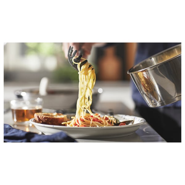 Kitchen scene: chefs serving spaghetti onto a plate using a large saucepan. The pan has a detachable handle.