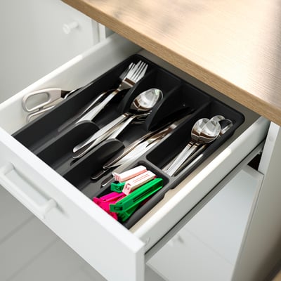 Open kitchen drawer showing organised cutlery tray with sections for forks, spoons, knives, and colourful pens.