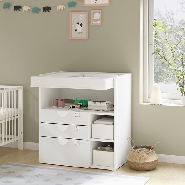 Modern white nursery changing table with shelves and drawers, featuring baby accessories and decor.