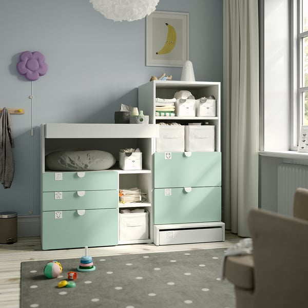 Modern nursery with mint green IKEA SMÅSTAD storage & changing table, baby essentials, grey rug, toys, curtain, large window.