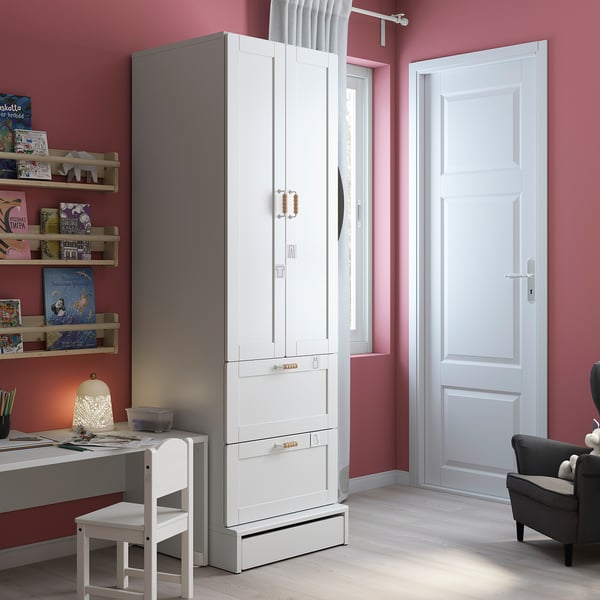 Modern kids room with SMÅSTAD white wardrobe, shelves, and desk. Pink walls, wooden floor, and cosy chair.