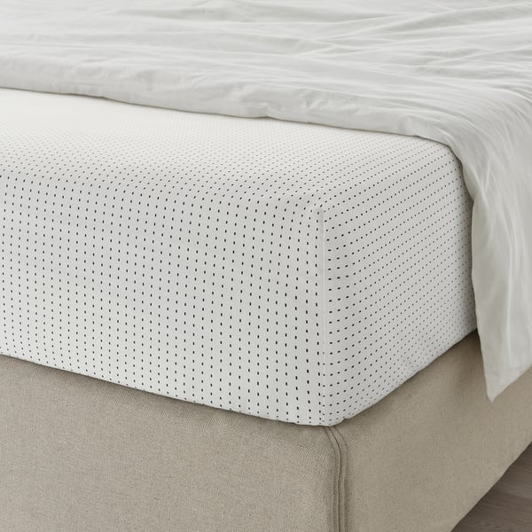 A neatly made bed with a white dot-patterned SMÅVÄNDEROT sheet set showcasing elastic edging on the fitted sheet.