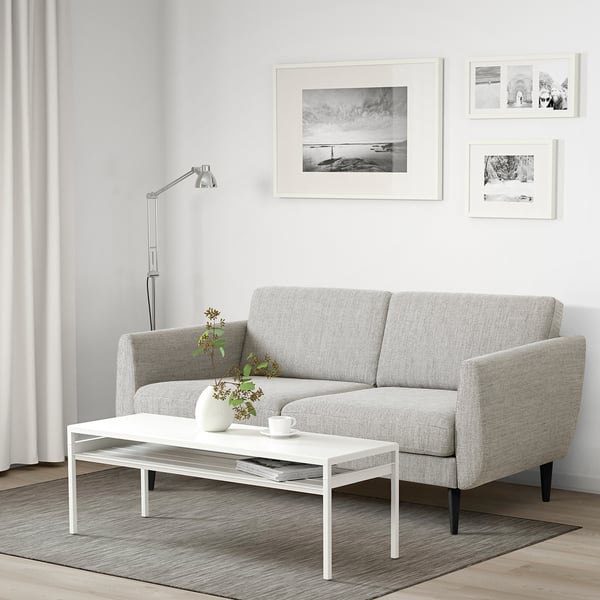 Grey retro sofa with soft cushions and cone legs, under black & white art, near tall lamp in minimalist living room.