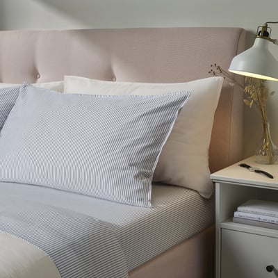 Bed with king size SOLFIBBLA light beige striped bedding. Topped with white pillows and a pinkish headboard. Grey bedside table nearby.