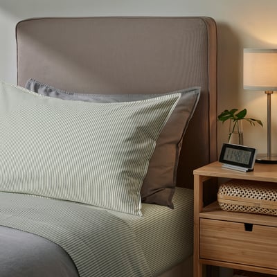 Brown SOLFIBBLA bedding with striped pillow, cosy headboard, bedside table, lamp, clock.