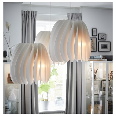Three sleek, white, modern pendant lights hang near a window. They feature a scalloped, ribbed design and emit a warm light.