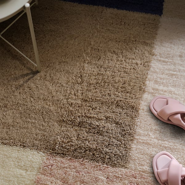 Shows a soft, hand-woven wool rug with multicoloured patterns. A pair of pink sandals nearby reminds us its cosy for walking.