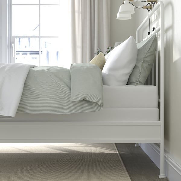 White metal bed with striped bedding, bright window light.