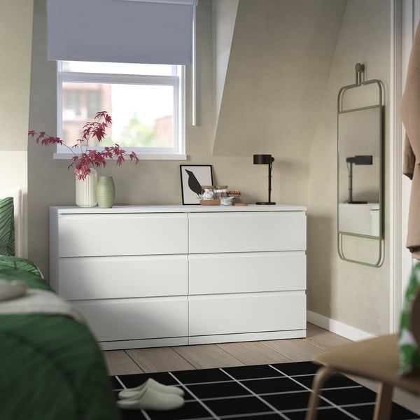 Modern bedroom with white STORKLINTA chest, sleek design, smooth drawers, top decor, and green plant.