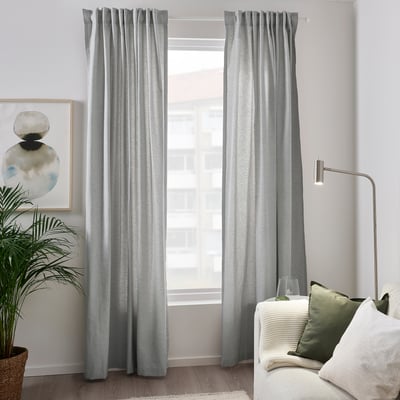 Modern living room with grey curtains near white couch & green pillows. Decor includes plant & abstract art.