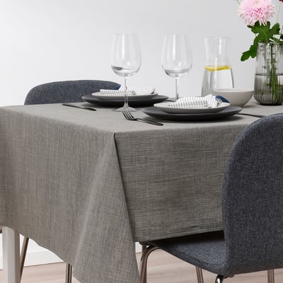 Table set with grey SVARTSENAP cloth, plates, cutlery, glasses, carafe, and flower vase.