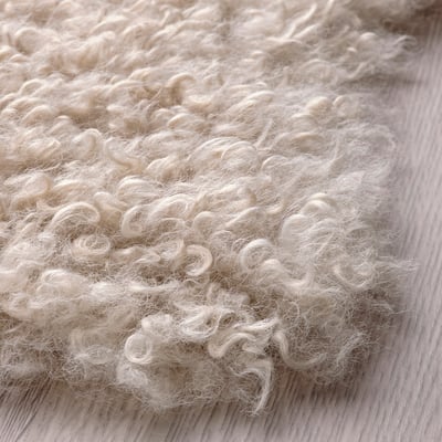 Soft, curly white rug on wooden floor; cosy, textured