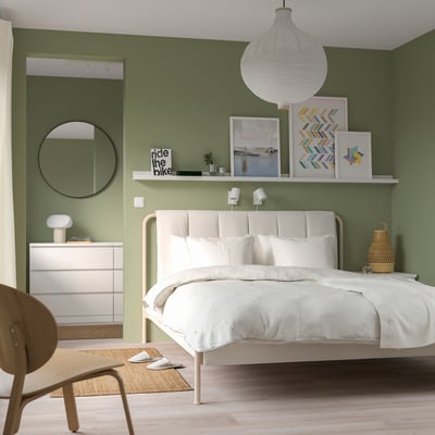 Modern bedroom with TÄLLÅSEN white bed, green walls, wooden chair, & decorations. Bed has padded headboard & adjustable base.