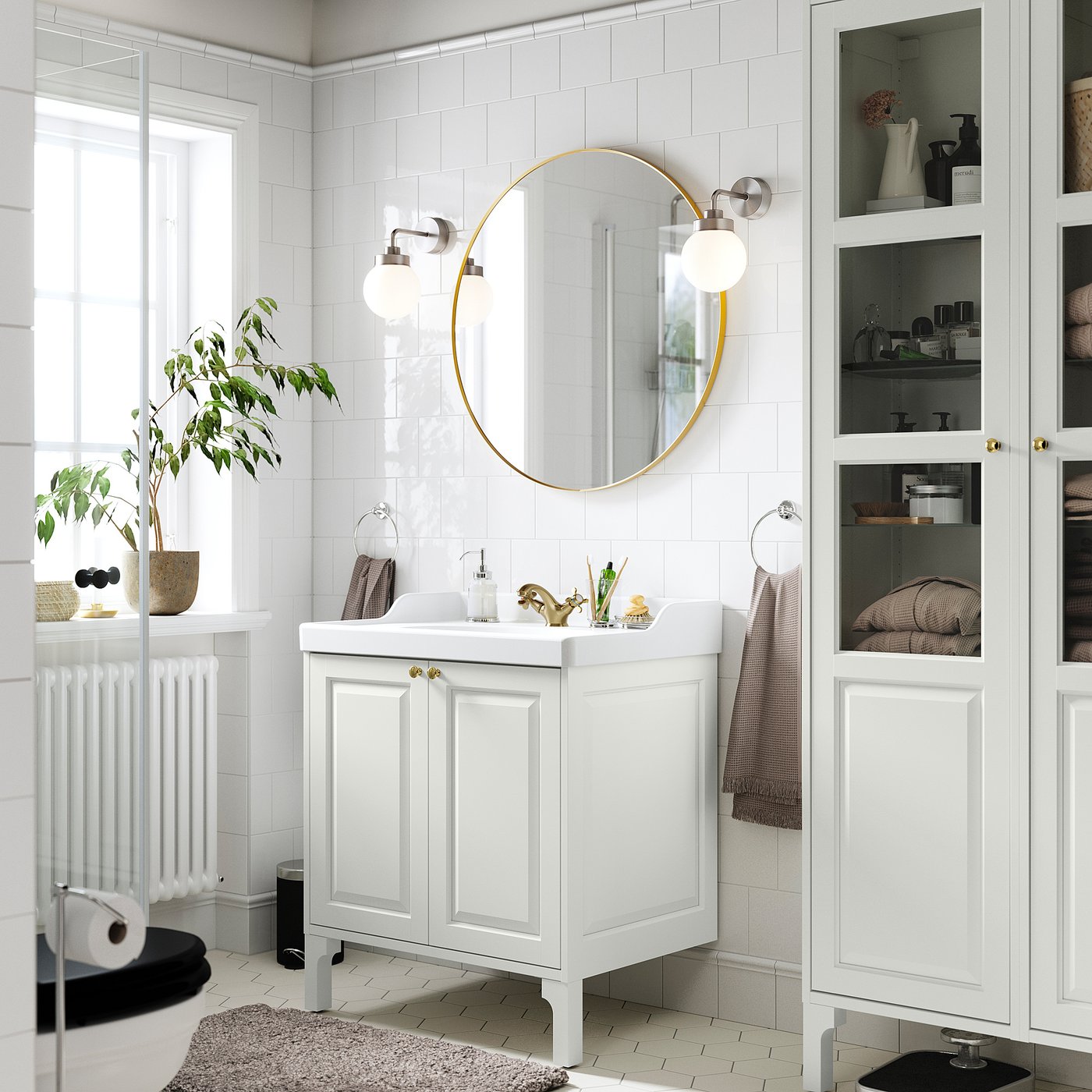 Modern white bathroom with TÄNNFORSEN cabinet and mirror. Gold accents, plants, and towels. Tall cabinet and sink against tiled wall.