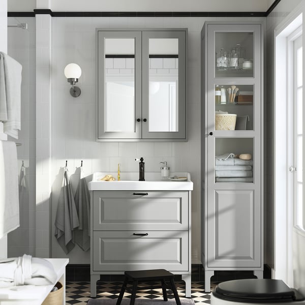 Modern bathroom with TÄNNFORSEN light grey vanity, sink, mirror cabinet, tall storage, and black stool. Clean, sophisticated look.