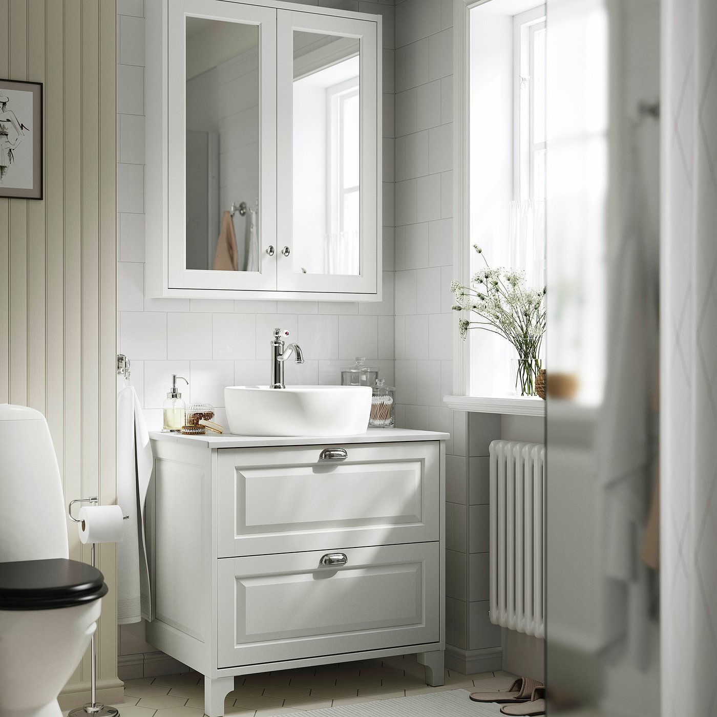 White TÄNNFORSEN vanity with round basin, marble top, mirror cabinet, window, radiator with flowers.