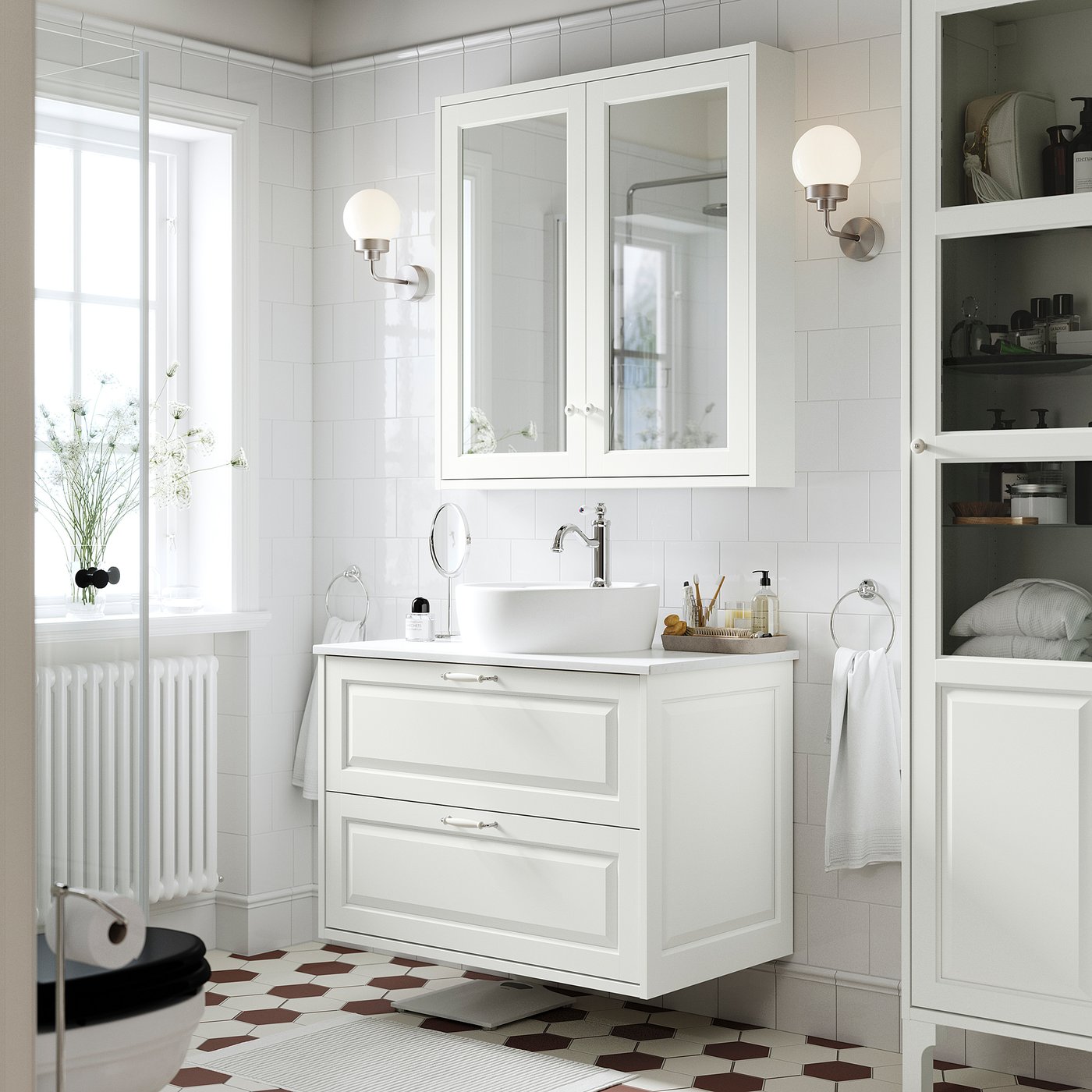 Modern bathroom with TÄNNFORSEN vanity, sink, mirror, and shelves. Wall-mounted washstand and drawers. Brown tiles, lights, and towels.