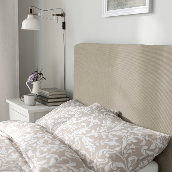 Cosy bed with large headboard, patterned bedding, and bedside table with books and flowers.